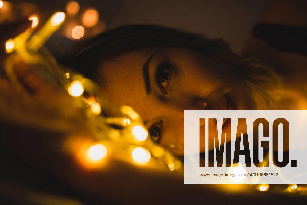 From above young beautiful woman in underwear lying in bed surrounded by light garland, Model released