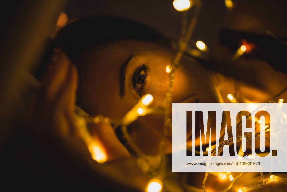 From above young beautiful woman in underwear lying in bed surrounded by light garland, Model released