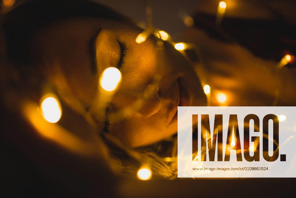From above young beautiful woman in underwear lying in bed surrounded by light garland, Model released