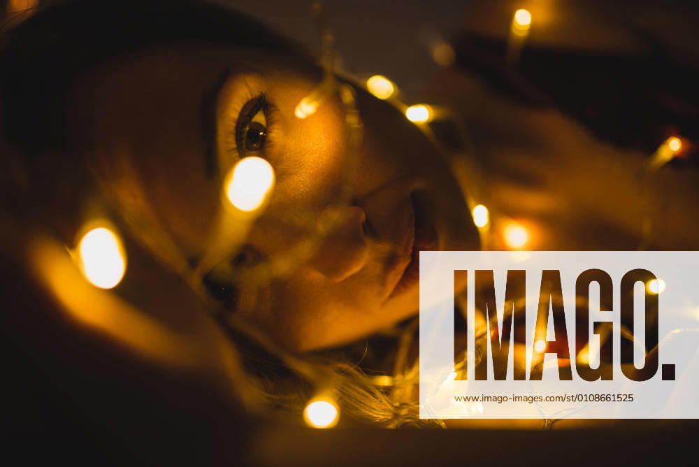 From above young beautiful woman in underwear lying in bed surrounded by light garland, Model released