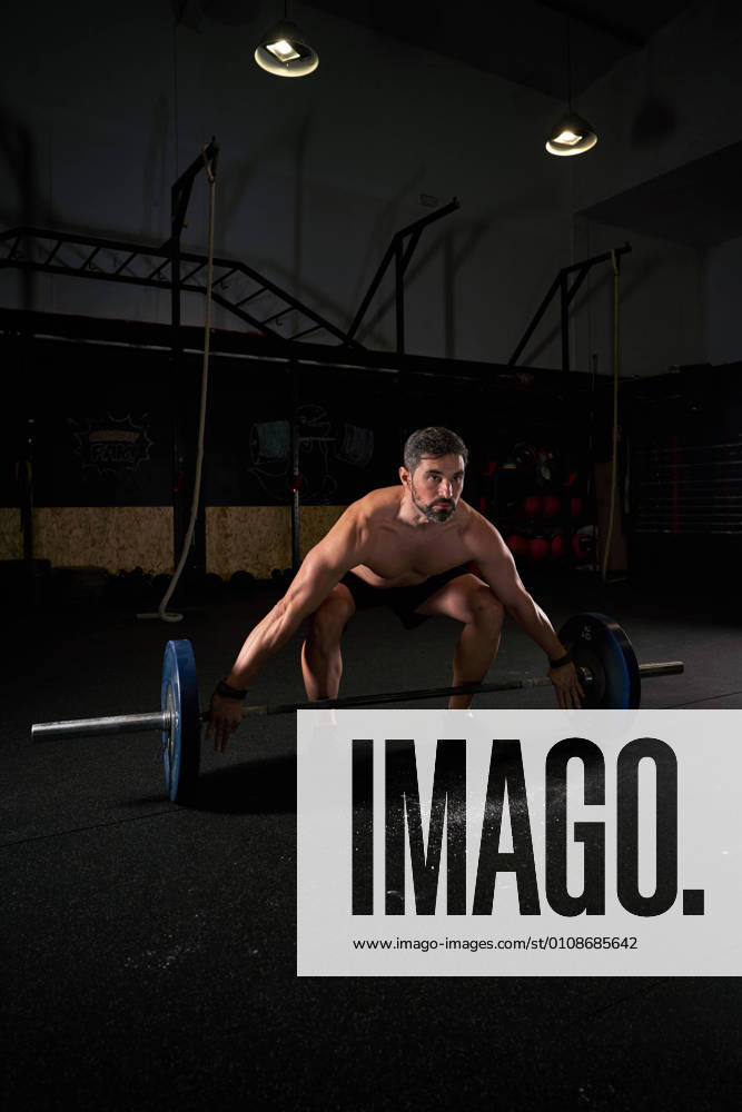 Strong man with barbell with weights in his hands doing strength exercises in the gym with magnesium in his hands. Young athlete practicing multidisciplinary training