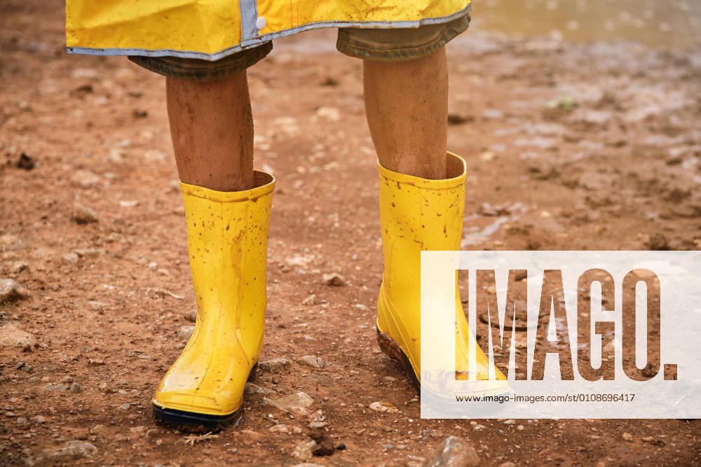 Detail of some legs with yellow dirty muddy water boots in the middle of a path in the forest, Model released