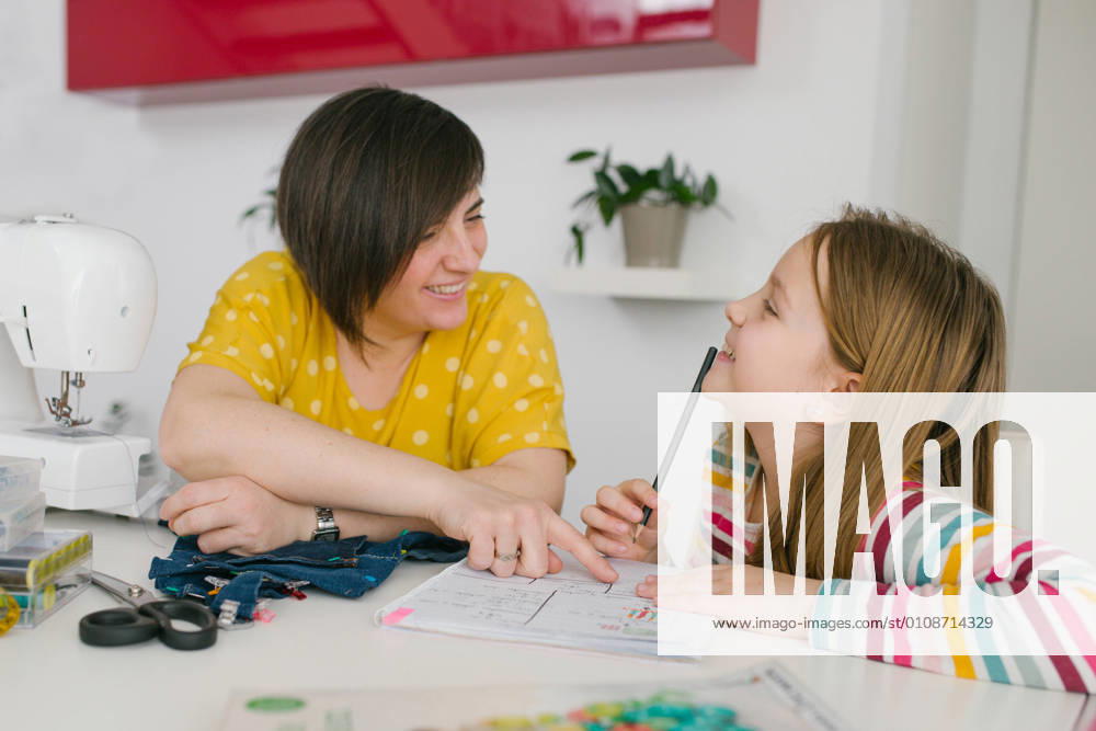 IMAGO Creative: Gesellschaft, Integration IMAGO Creative: Internationaler Frauentag, Mental Load und Care-Arbeit Happy adult woman smiling and helping girl with homework assignment while sewing garment at home