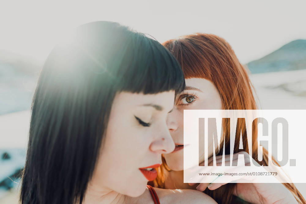 Side view of modern sensual lesbian couple in love embracing while standing in back lit in snowy field at countryside, Model released