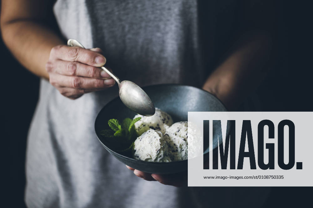 Crop view of anonymous woman with spoon in hand and holding bowl with stracciatella ice cream balls decorated with mint leaves