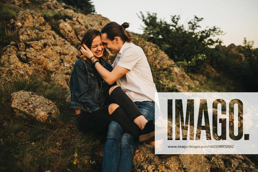 Young man kissing girlfriend in cheek while sitting together on slope of rocky mountain, Model released