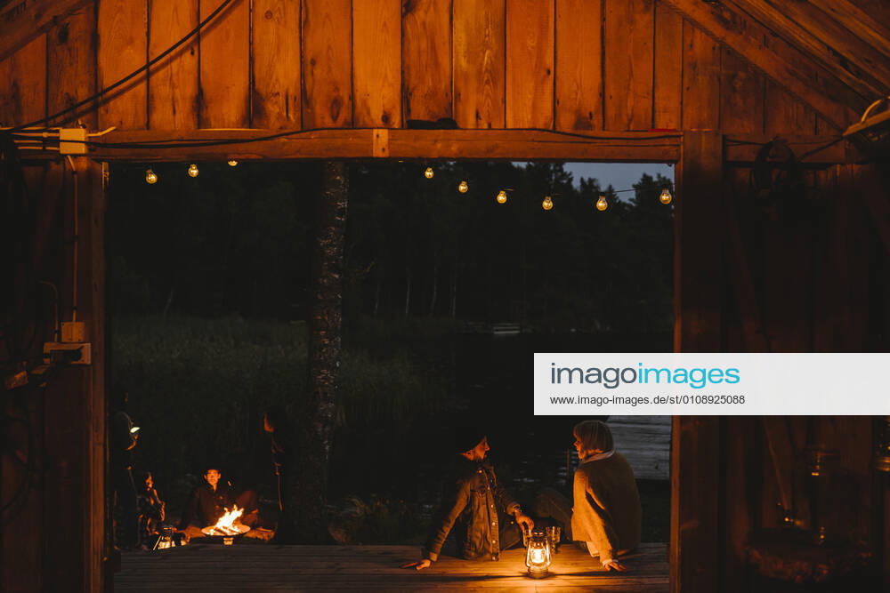 Couple talking while friends sitting by fire pit during sunset Sweden, Stockholm, model released, property released
