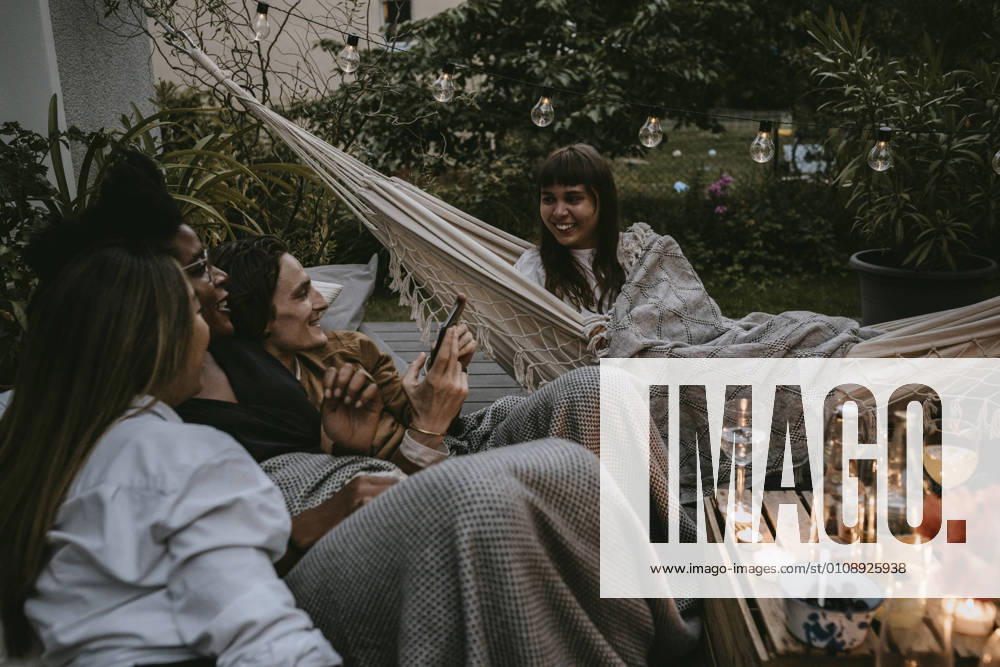 IMAGO Creative: Landleben - Essen Smiling woman on hammock with friends enjoying during social gathering Sweden, Stockholm, model released, property released