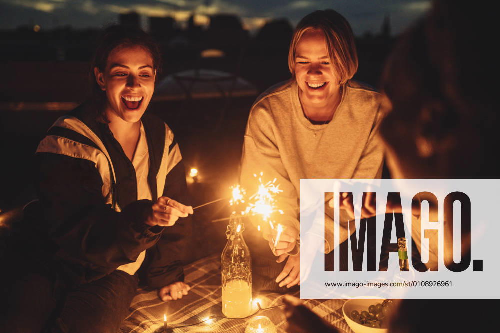 IMAGO Kreativ: Urbane Kultur - Sommer auf den Dächern Cheerful female with friends igniting sprinkler on building rooftop at night Germany, Berlin, model released, property released