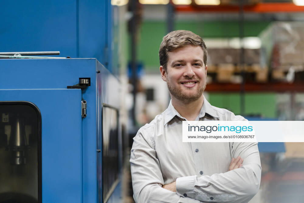 Happy businessman with arms crossed standing in manufacturing industry model released Symbolfoto property released DIGF13133