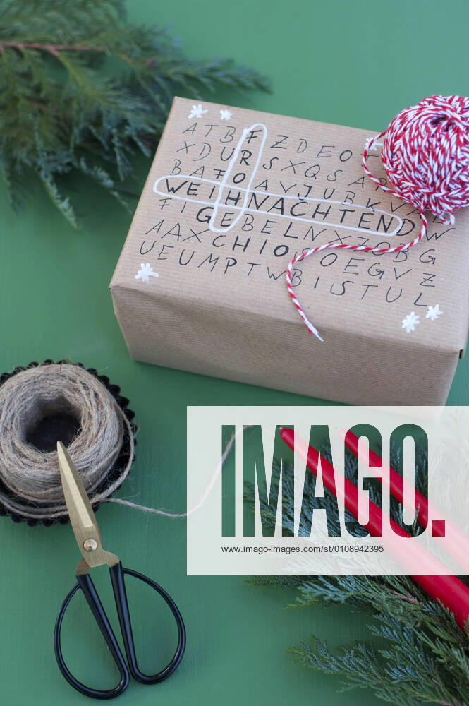 IMAGO Creative: Weihnachten, DIY, Geschenke verpacken - Nachhaltigkeit Scissors, string and word search puzzle on wrapped Christmas present GISF00714