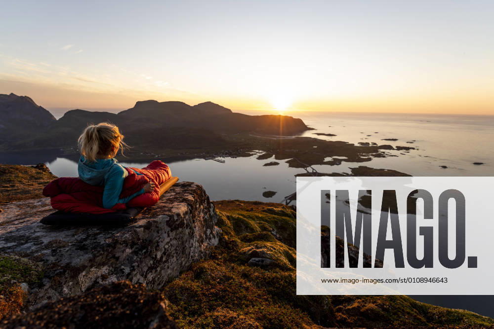 Hiker admiring sunset view while lying in sleeping bag at Volandstinden, Lofoten model released Symbolfoto MALF00248
