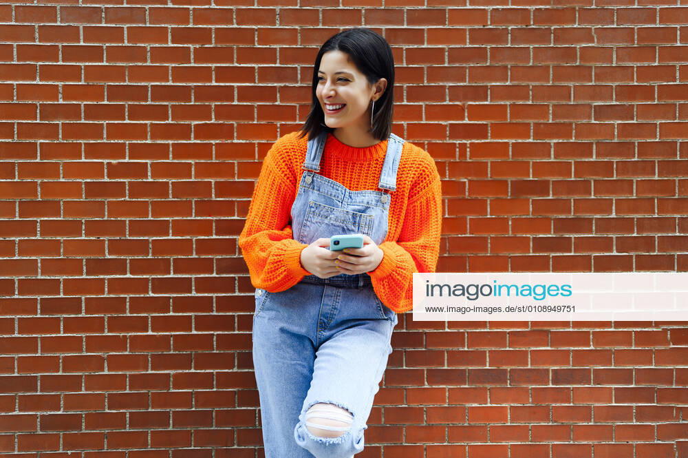 Smiling woman looking away while standing against brick wall model released Symbolfoto PGF00214