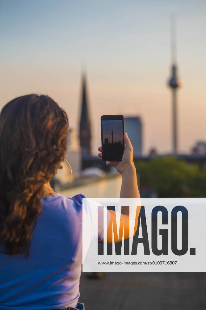 IMAGO Kreativ: Urbane Kultur - Sommer auf den Dächern Woman photographing through smart phone while standing on rooftop model released Symbolfoto NGF00712