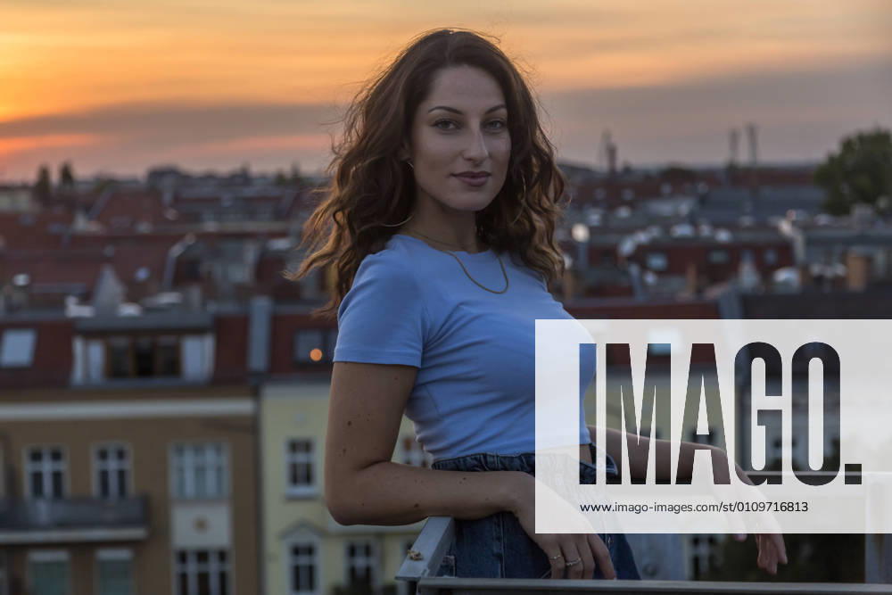 IMAGO Kreativ: Urbane Kultur - Sommer auf den Dächern Smiling woman standing on rooftop against sky during sunset model released Symbolfoto NGF00718
