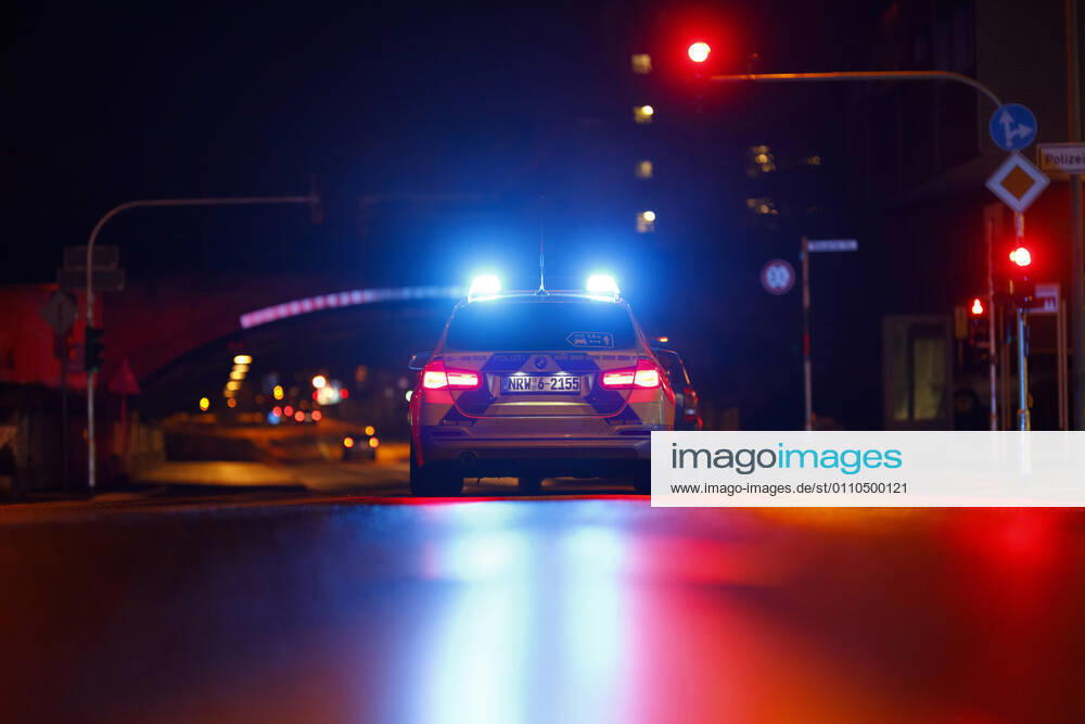 Ein Polizeiauto kontrolliert einen Wagen an einer Ampel. (Themenbild, Symbolbild) Köln