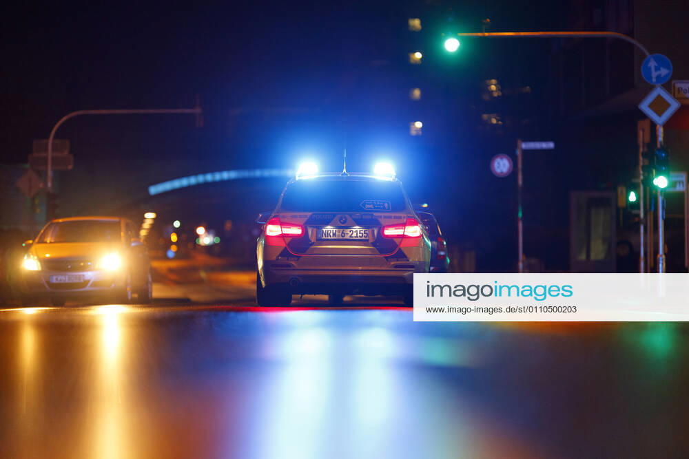 Ein Polizeiauto kontrolliert einen Wagen an einer Ampel. (Themenbild, Symbolbild) Köln