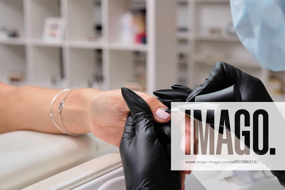 Closeup of crop anonymous master in gloves using metal cuticle pusher while doing manicure for female client in beauty salon, Model released, Property released