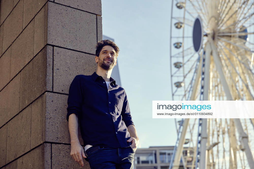 Thoughtful businessman standing with hands in pockets against wall and ferris wheel in city model released Symbolfoto RHF02584