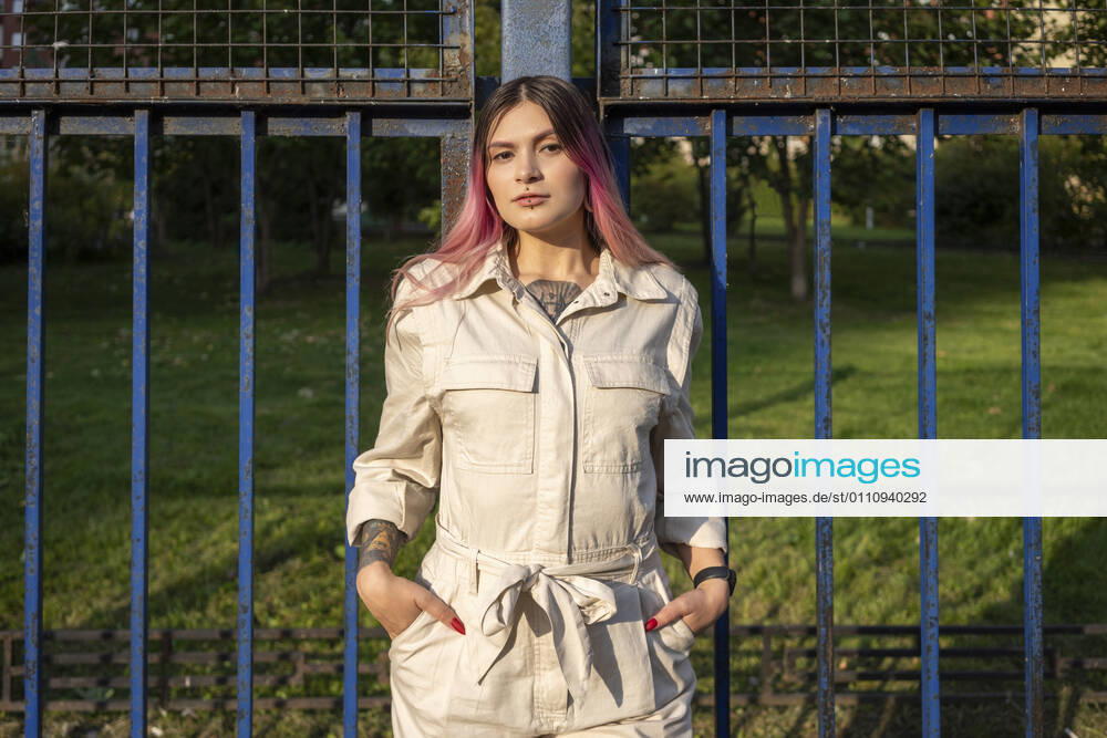 Stylish young woman with hands in pockets against fence on sunny day model released Symbolfoto VPIF03326