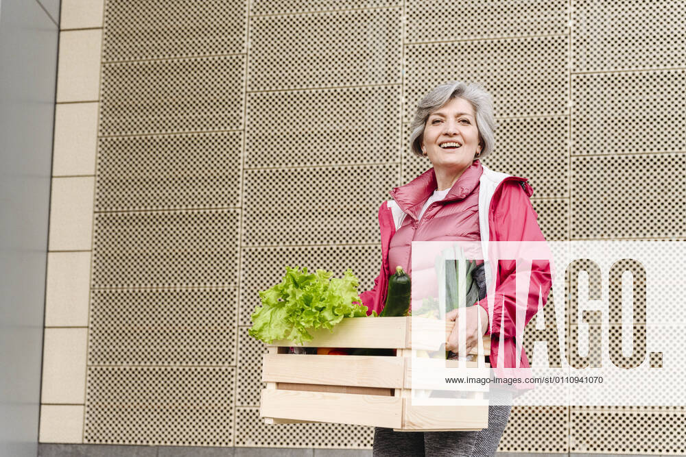 Happy mature woman with food crate against iron pattern wall model released Symbolfoto VYF00371