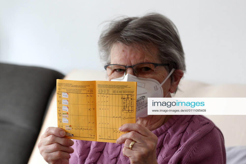Winden Themenbild - Coronavirus, Coronapandemie - Patientin einer Risikogruppe mit internationale Impfbescheinigung, Prophylaxebescheinigung, Impfpass, Impfbuch Themenbild - Coronavirus, Coronapandemie - Patientin einer Risikogruppe mit internationale Impfbescheinigung, Prophylaxebescheinigung, Impfpass, Impfbuch Coronavirus, Coronapandemie - Impfpass, Impfbuch, Impfbescheinigung, Impfdokument, internationale Impfbescheinigung, Prophylaxebescheinigung. Eine ältere Person, Rentnerin, einer Risikogruppe, mit 80 Jahren, sitzt in ihrem Wohnzimmer auf der Couch, Sofa und hält ihren gelben Impfpass für die bevorstehende Corona Schutzimpfung in der Hand, in den älteren, runzligen Fingern ihrer Händen. Model release Vertrag liegt vor. Model