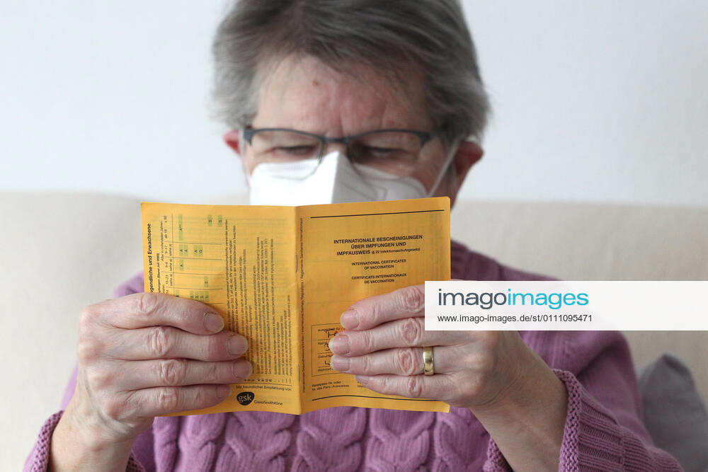 Winden Themenbild - Coronavirus, Coronapandemie - Patientin einer Risikogruppe mit internationale Impfbescheinigung, Prophylaxebescheinigung, Impfpass, Impfbuch Themenbild - Coronavirus, Coronapandemie - Patientin einer Risikogruppe mit internationale Impfbescheinigung, Prophylaxebescheinigung, Impfpass, Impfbuch Coronavirus, Coronapandemie - Impfpass, Impfbuch, Impfbescheinigung, Impfdokument, internationale Impfbescheinigung, Prophylaxebescheinigung. Eine ältere Person, Rentnerin, einer Risikogruppe, mit 80 Jahren, sitzt in ihrem Wohnzimmer auf der Couch, Sofa und hält ihren gelben Impfpass für die bevorstehende Corona Schutzimpfung in der Hand, in den älteren, runzligen Fingern ihrer Händen. Model release Vertrag liegt vor. Model