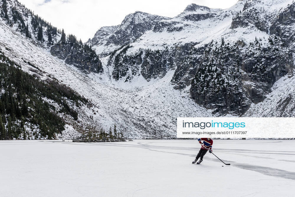 IMAGO Creative: Alternativer Wintersport Man playing hockey near snowy mountains on frozen lake in Canada Canada, British Columbia, Pemberton CR_PSFZ210201-623643-01 ,model released, Symbolfoto