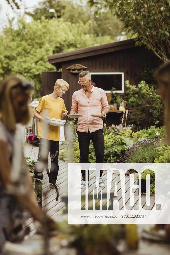 IMAGO Creative: Landleben - Essen Father and son walking with bowl and plate in back yard during social event Sweden, Gothenburg, model released, property released