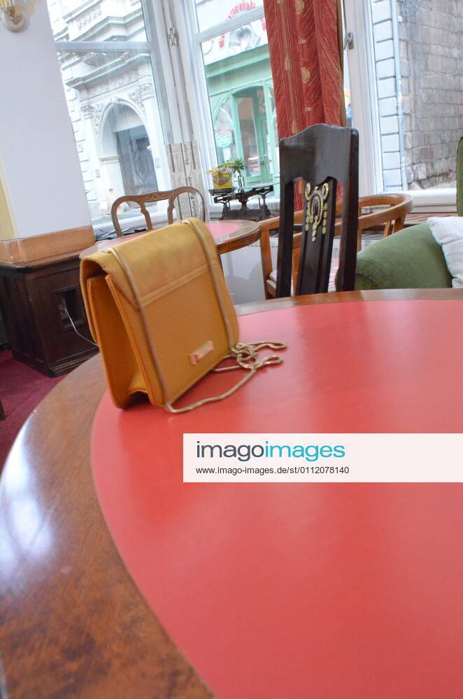Eine junge Frau in einer gelben Jackeund einem grünen Kleid sitzt mit einer gelben Handtasche in einem Cafe restaurant. Symbolfoto.