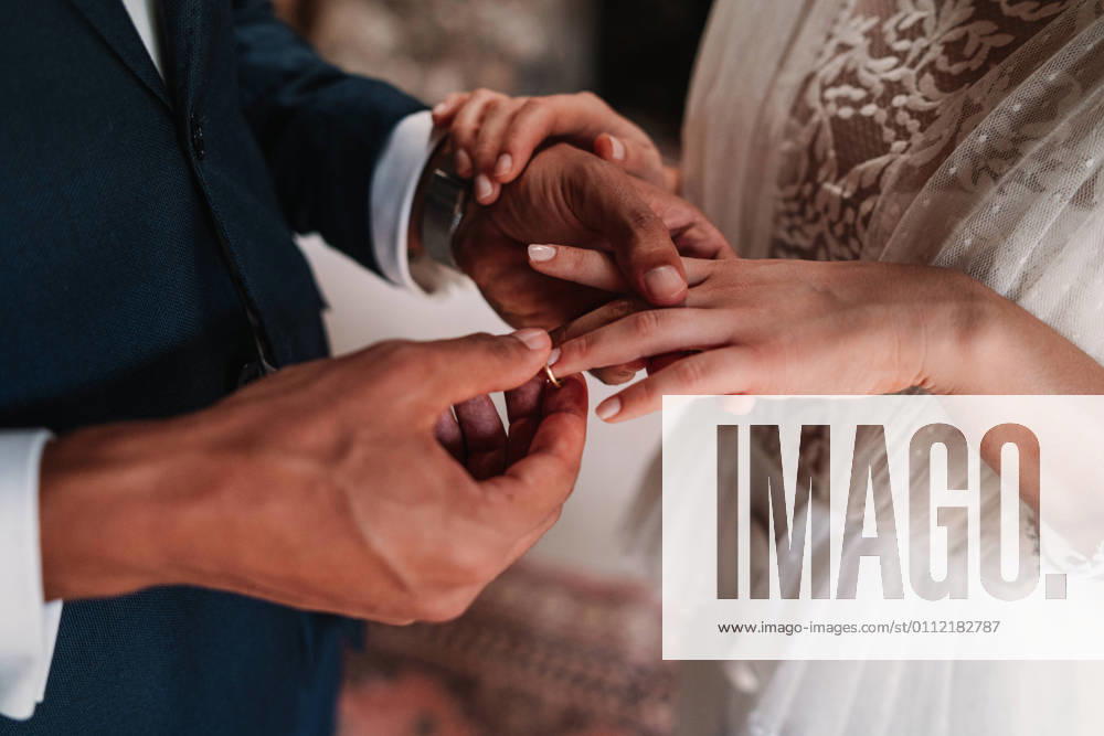 High angle side view of cropped unrecognizable ethnic groom putting ring on finger of bride in fancy wedding gowns holding hands gently with affection