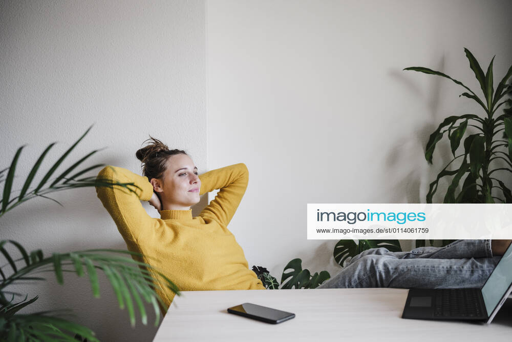 Smiling woman with hands behind head relaxing while sitting by table at home model released Symbolfoto property released EBBF02409