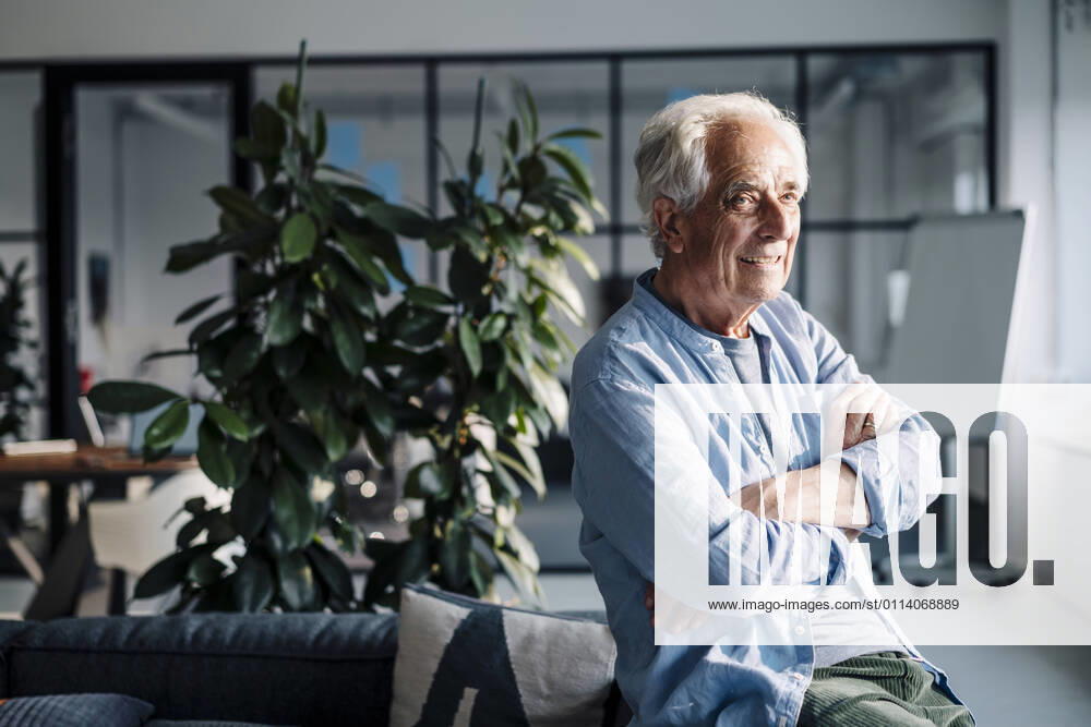 Smiling businesswoman with arms crossed looking away while sitting at office model released Symbolfoto property released GUSF05116