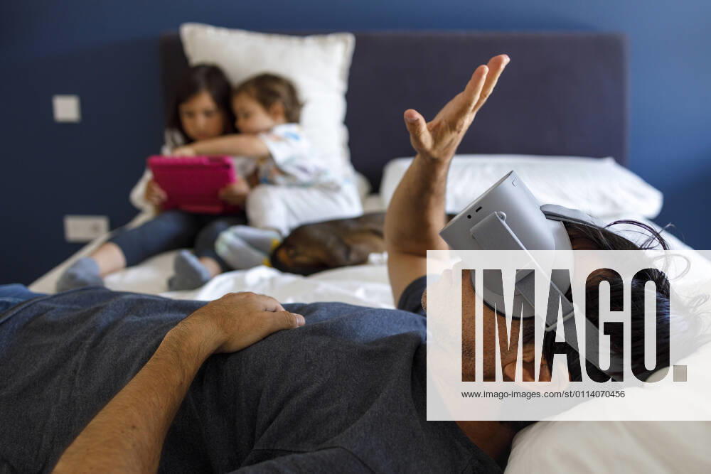 Man with virtual reality simulator gesturing while siblings using digital tablet on bed at home model released Symbolfoto property released IFRF00399