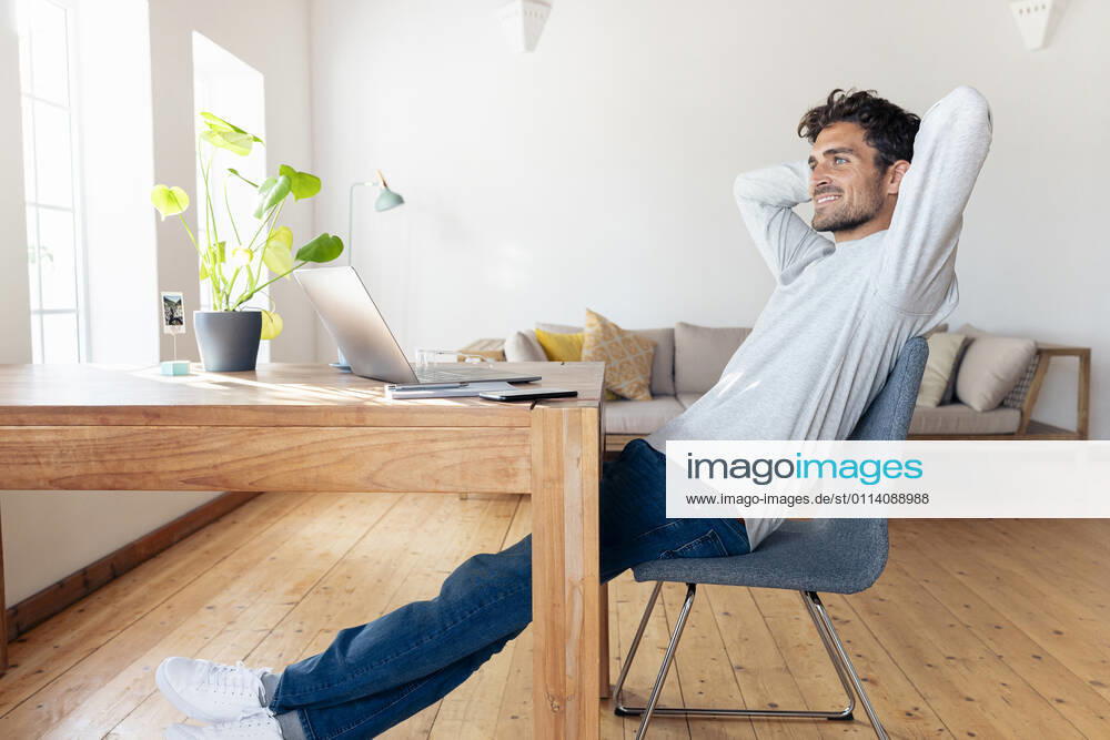 Smiling man with hands behind head relaxing while sitting on chair at home model released Symbolfoto property released SBOF02408