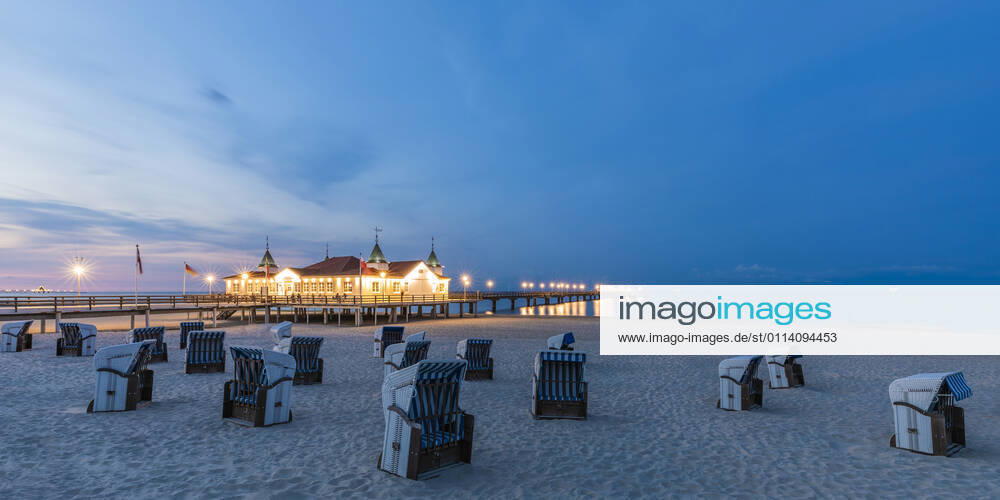 Germany, Mecklenburg-Western Pomerania, Heringsdorf, Hooded beach chairs on empty beach at dusk with illuminated Ahlbeck Pier in background WDF06495
