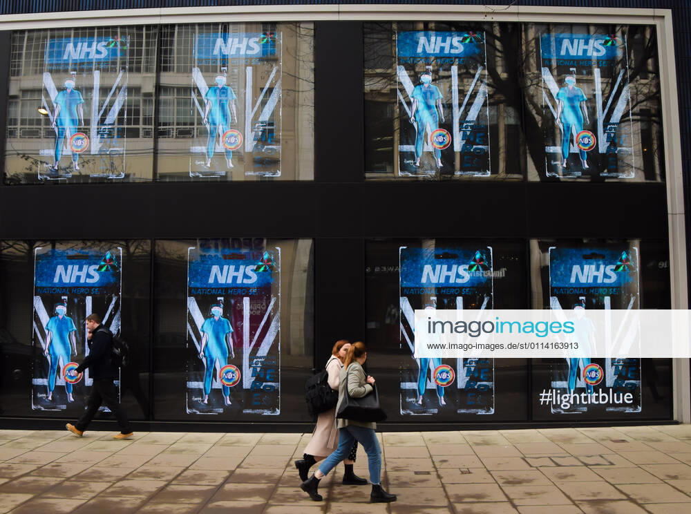 People walk past screens displaying NHS National Hero at the Flannels store on Oxford Street in London..The screens at the store are currently showing a series of artworks as part of the LightItBlue campaign in support of the NHS. London United Kingdom - ZUMAs197 20210225_zaa_s197_087