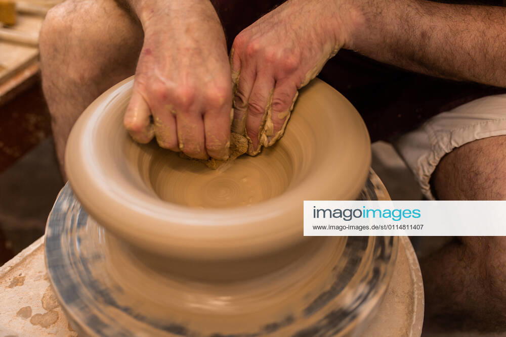Crop unrecognizable sculptor with equipment giving shape while sculpting with brown clay on throwing wheel, Model released