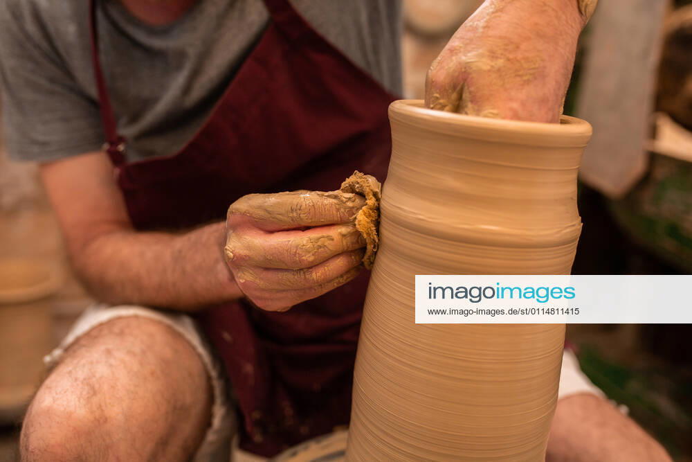 Crop unrecognizable sculptor with equipment giving shape while sculpting with brown clay on throwing wheel, Model released