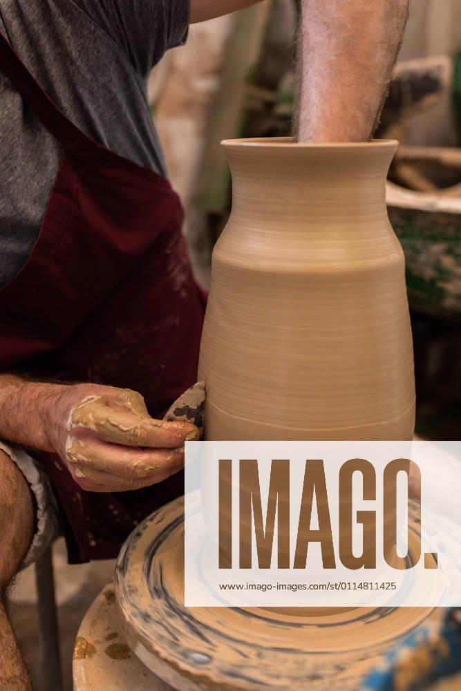 Crop unrecognizable sculptor with equipment giving shape while sculpting with brown clay on throwing wheel, Model released