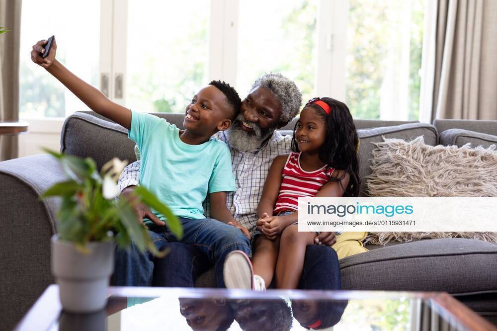 Senior African American man and his grandchildren at home Senior African American man and his grandchildren enjoying their time at home together, sitting on a couch, embracing, smiling, using a smartphone, taking a selfie, model released, , property released, Cape Town, South Africa, 19.02.2020, 1340053.jpg, people,family,grandfather,granddad,granddaughter,grandson,siblings,brother,sister,childhood,together,closeness,interacting,sitting,couch,holding,using,phone,mobile phone,smartphone,connection,communication,taking,photo,photograph,selfie,real people,home,house,domestic life,lifestyle,enjoying,free time,leisure,relaxing,weekend,summer,sunny,love Child,Girl,Female,Mixed-Race,Mid Adult,Man,Male,Black Indoors,Front view,Day,Three Quarter Le