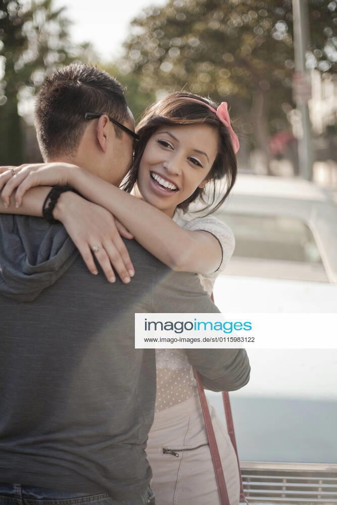 Smiling girlfriend embracing boyfriend standing against car model released Symbolfoto AJOF01247