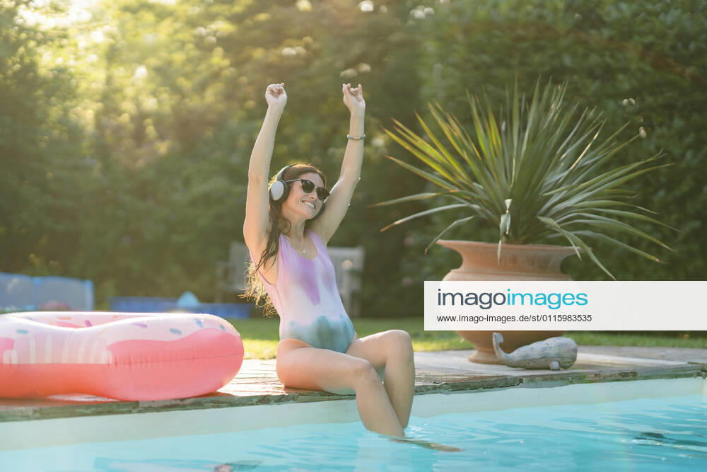 Cheerful woman in swimwear enjoying music while sitting at pool model released Symbolfoto property released AKLF00065