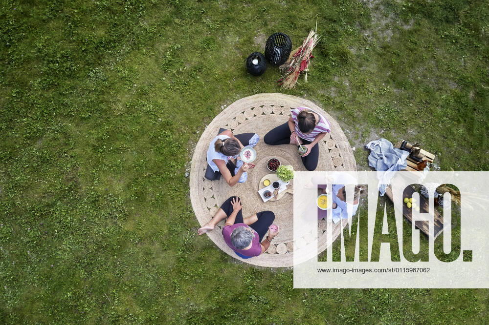 IMAGO Creative: Jahreszeit Frühling, Picknick Caucasian female friends having food while sitting on meadow model released Symbolfoto CVF01664