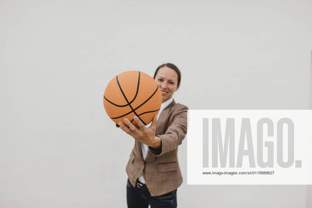 Playful female professional with basketball standing against white wall while taking break model released Symbolfoto DMGF00517