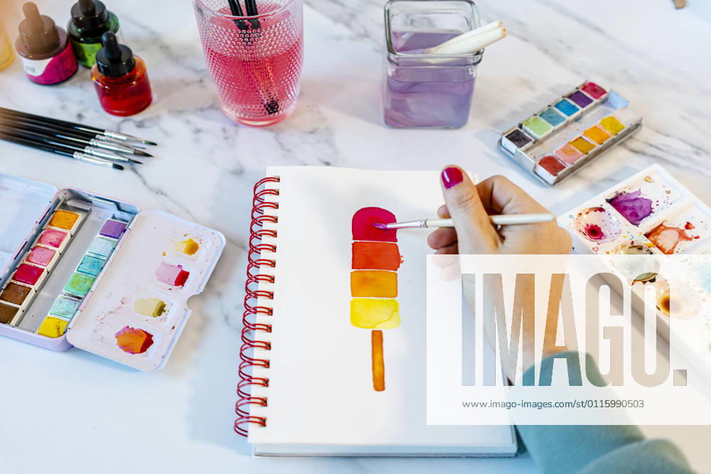 Woman painting popsickle ice cream with watercolor in book on table model released Symbolfoto property released GEMF04682