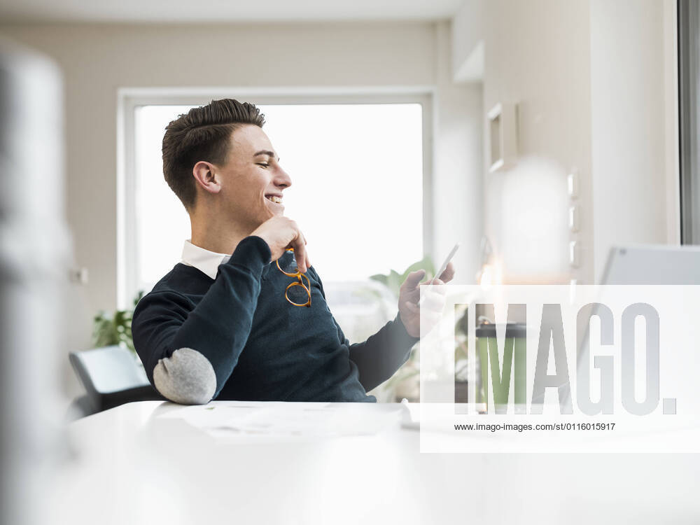 IMAGO Creative: Kreative Renaissance -- der junge Entrepreneur Smiling male entrepreneur surfing net through smart phone while sitting at home office model released Symbolfoto property released UUF22864