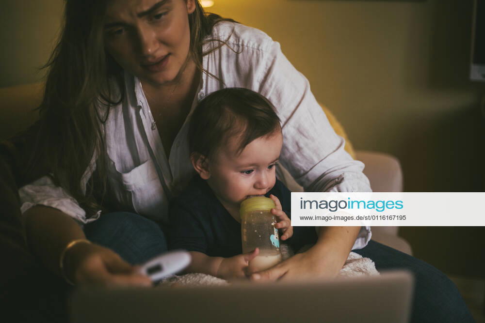 Mother checking temperature of baby girl while taking advice through online consultation at home during pandemic Sweden, Stockholm, model released, property released