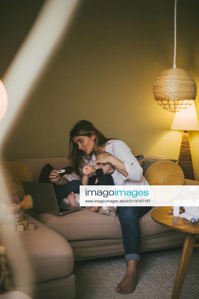 Mother checking temperature of baby girl while taking advice through online consultation at home during COVID-19 Sweden, Stockholm, model released, property released
