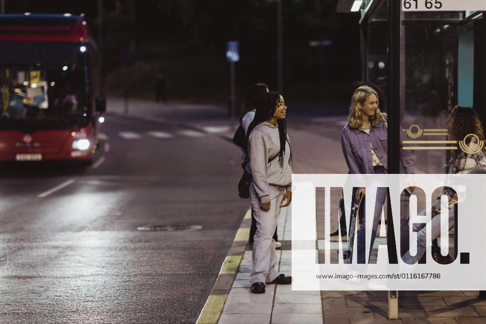 IMAGO Creative, Jahreszeit Sommer, Sommer in der Stadt IMAGO Creative: Gesellschaft, Integration IMAGO Creative: Landleben - Alfresco, Draußen Female friends sitting on bus stop at night Sweden,Stockholm, model released